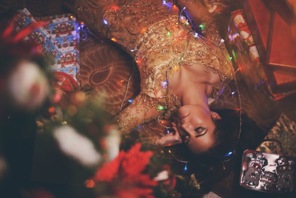 漂亮的女人穿着金色的衣服躺在家中附近的地板上，中间夹着礼物。健美的照片。新年的概念图片下载