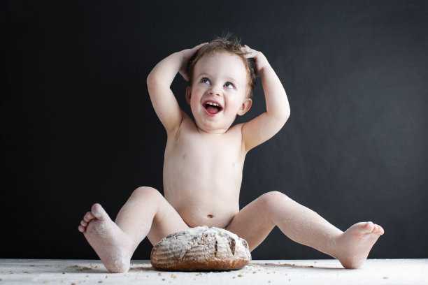 快乐的男孩在面包店的桌子上玩着自制的新出炉的面包和面粉。背景黑色墙体混凝土图片下载