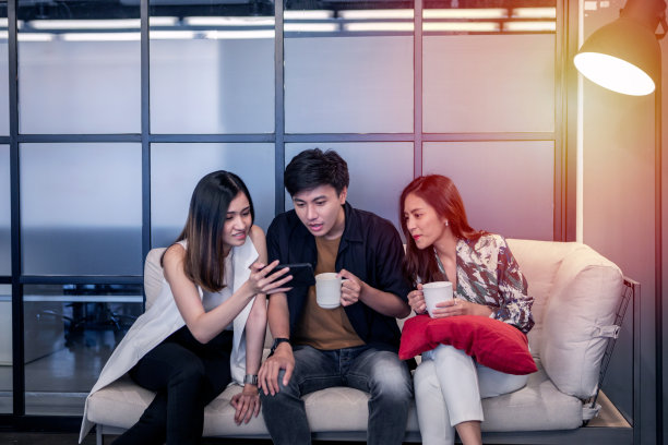 年轻的亚洲商业男人和女人享受在办公室的咖啡休息和看照片的智能手机图片下载
