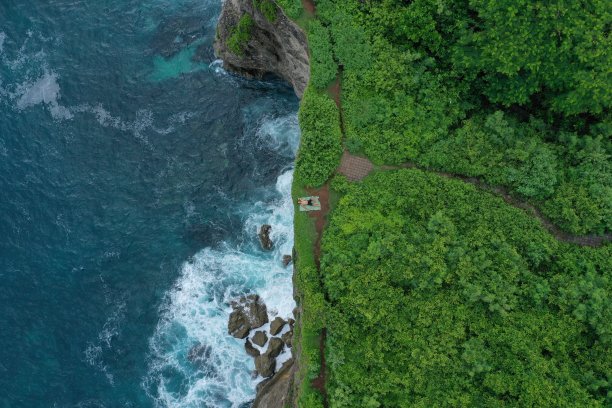 在印度尼西亚巴厘岛的乌鲁瓦图，一个人躺在蓝色的印度洋上的绿色悬崖上，浪花翻滚。航拍照片，一名男子躺在蓝色的印度洋上的绿色悬崖上，浪花翻腾，印度尼西亚巴厘岛的乌鲁瓦图。图片下载