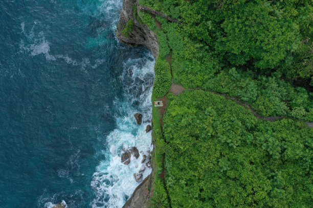 在印度尼西亚巴厘岛的乌鲁瓦图，一个人躺在蓝色的印度洋上的绿色悬崖上，浪花翻滚。航拍照片，一名男子躺在蓝色的印度洋上的绿色悬崖上，浪花翻腾，印度尼西亚巴厘岛的乌鲁瓦图。图片下载