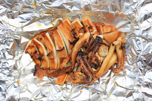烤鱿鱼在褶皱的锡箔背景。图片下载