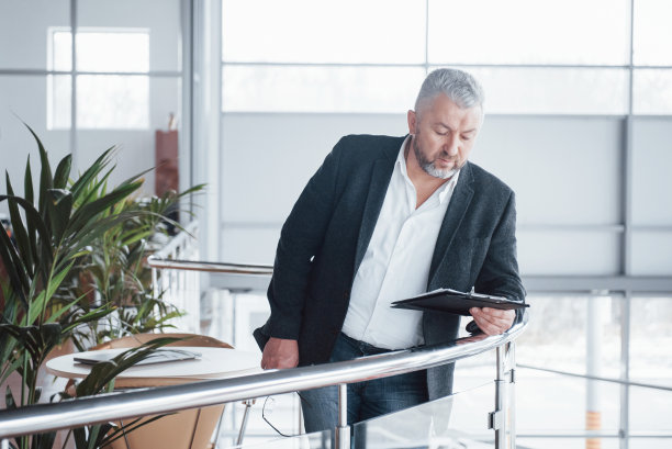 宽敞的房间里摆放着植物和桌子，里面是资深商人的照片。持有和阅读文件图片下载