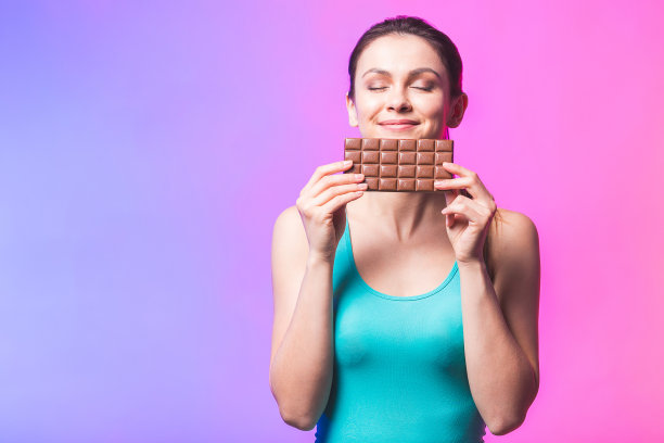 快乐年轻健康美丽的女士吃巧克力和微笑。女孩正在品尝香甜的巧克力。年轻女子与自然的化妆有乐趣和吃巧克力孤立的白色背景。图片下载