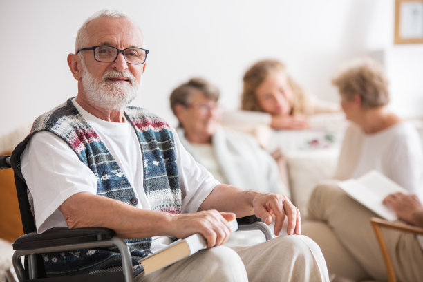 一名坐在轮椅上的老年男子，手里拿着一本书，摆姿势拍照图片下载