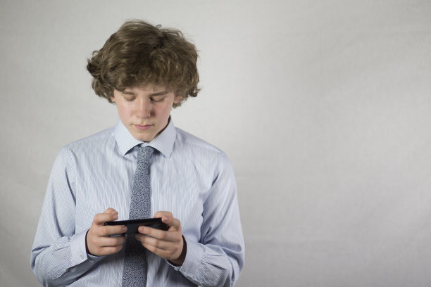 一个十几岁的男孩拿着智能手机，白色背景上是一个男生。图片下载