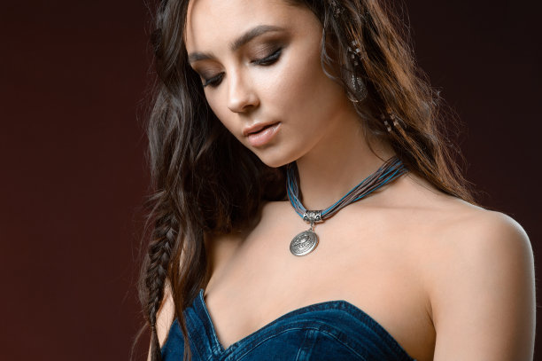 戴着项链、耳环和戒指的年轻女子。模型在珠宝。工作室照片在棕色的背景图片下载