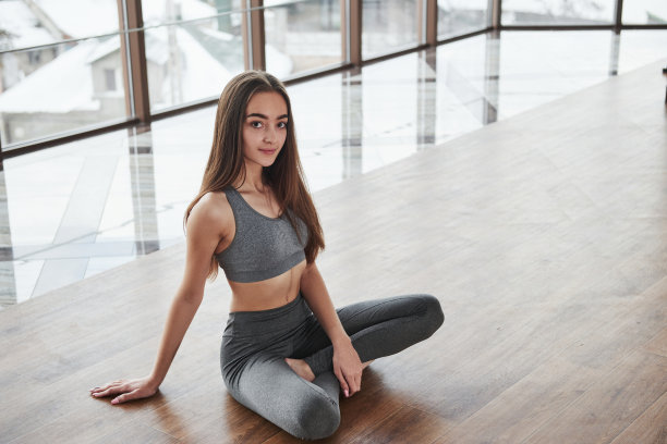 从上面的照片。轻松可爱的年轻女孩坐在地板上的健身房与大窗户图片下载