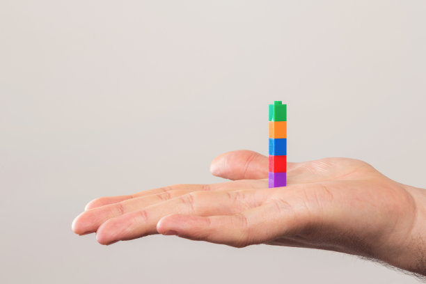 人的手和彩色的砖块越过白色的墙。图片下载