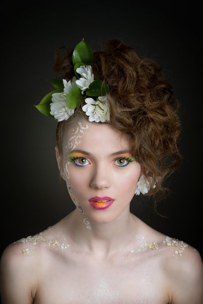 美丽的女人与深色头发在春天的风格与颜色面部艺术和鲜花摆姿势在工作室的黑暗背景图片下载