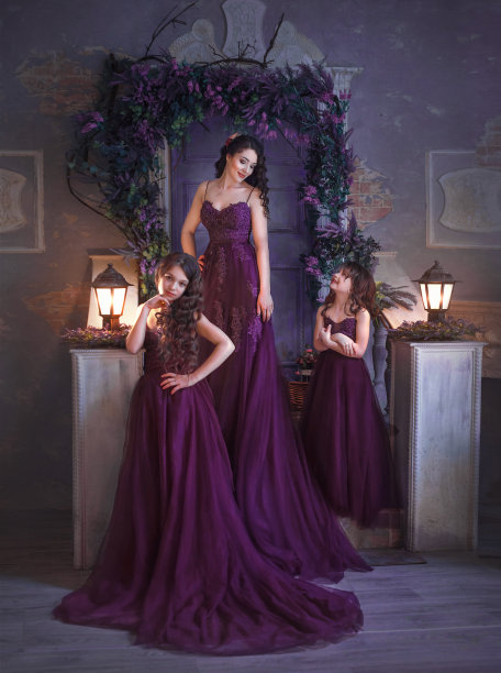 一个家庭。母亲和两个女儿穿着华丽的紫红色裙装，拖着长长的裙裾，在一个鲜花盛开的庭院里摆姿势。女孩们有长长的卷发。艺术照片图片下载