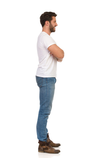 穿着牛仔裤和白色t恤的年轻人双臂交叉站在那里，看向别处。侧视图。图片下载