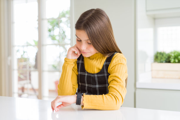 年轻漂亮的金发小女孩穿着休闲黄色毛衣在家看手表上的时间，放松和自信图片下载