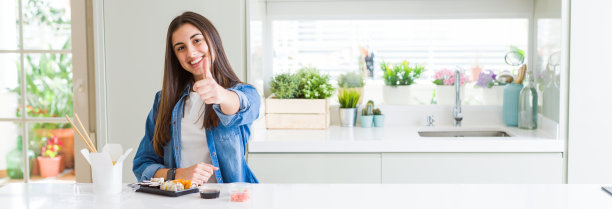 广角图片美丽的年轻女子吃送寿司做幸福的拇指向上手势与手。赞许的表情看着镜头，表示成功。图片下载
