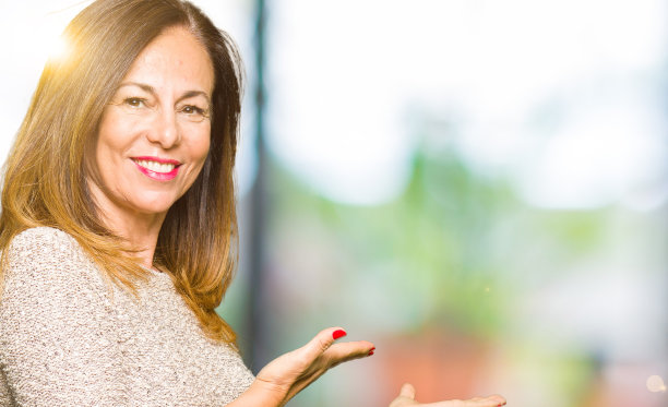 美丽的中年妇女穿着时尚的毛衣邀请进入自然的微笑与张开的手图片下载