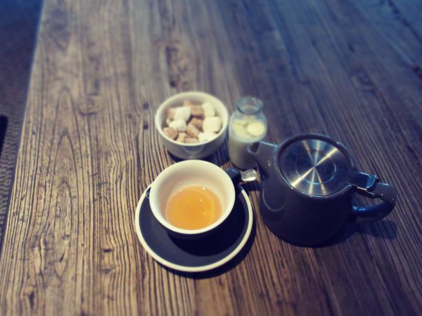 一张棕色的木桌，有茶壶、茶杯和茶托，一小碗方糖和牛奶图片下载