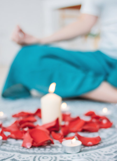 模糊的背景是一个女人在蜡烛和玫瑰花瓣前练习瑜伽图片下载