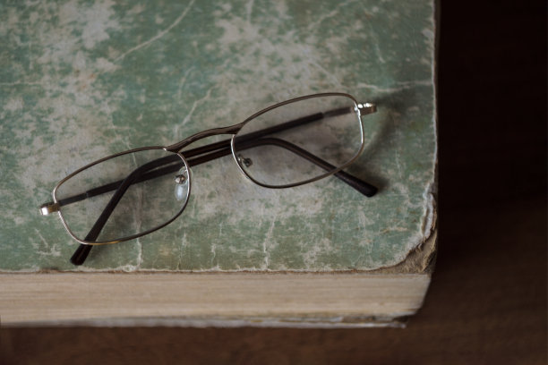 眼镜放在一本边角破损、封面破旧的旧书上。学习、阅读、教育的概念。俯视图图片下载