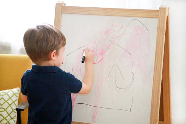 孩子是绘画和绘画与毛毡笔在纸上的木制画板艺术家画架儿童和儿童在家。的童年。可爱的小男孩，孩子在幼儿园用铅笔和彩色马克笔画画。图片下载