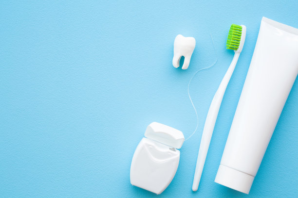 白色牙齿，牙膏管，绿色刷毛牙刷，蓝色背景的牙线盒。人的牙齿卫生。文字，引用，语录或标志的空白位置。特写镜头。图片下载