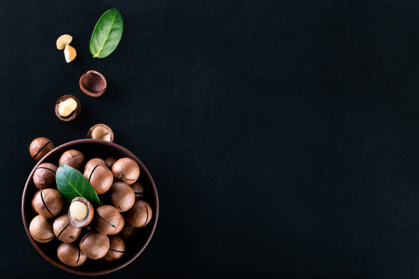 盘子里的澳洲坚果，谷物和叶子以黑色为背景图片下载