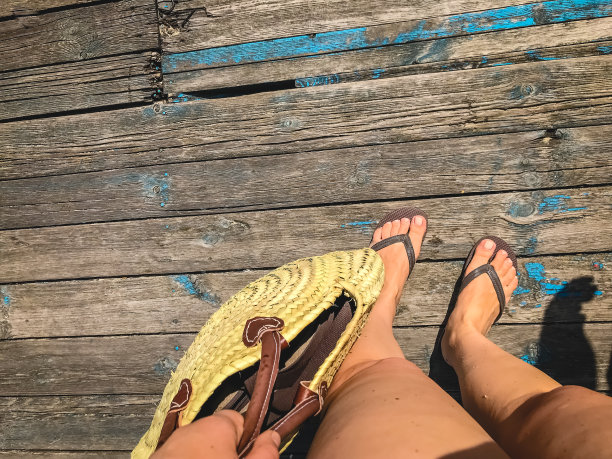俯视图，照片的腿在沙滩人字拖和一个稻草袋在一个木制旧地板上。度假、海滩、夏天的照片图片下载