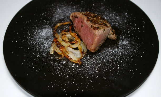 小菲力牛排和炸洋葱圈的开胃菜放在一个黑色的盘子里图片下载