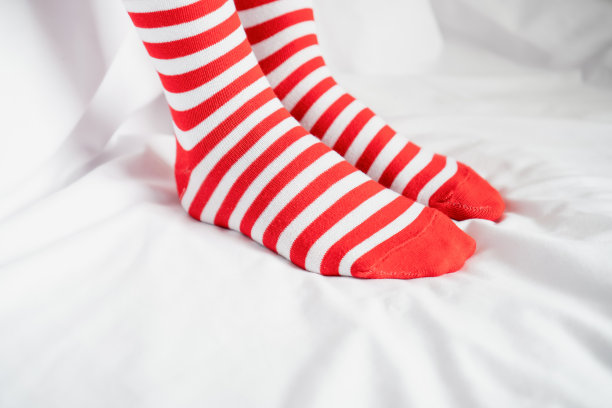 女人的双腿在袜子的颜色交替，侧身站在白色的织物地板上。图片下载