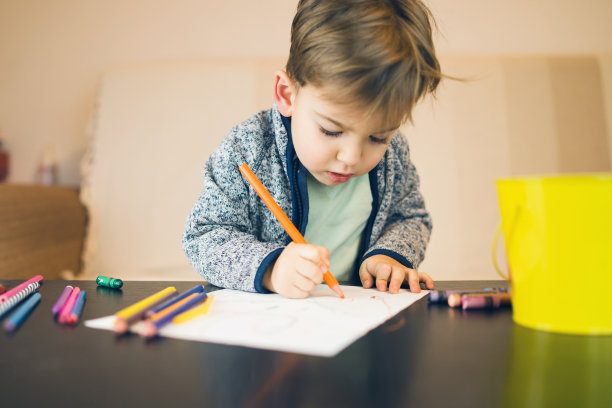 2岁小男孩的肖像，用蜡笔在白纸上写字，画画，在家里的桌子旁玩耍。图片下载