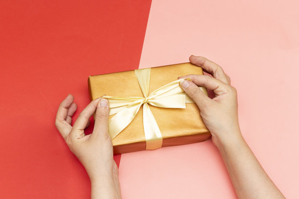 女性手握礼物在红、粉纸上。节日背景:生日，情人节，圣诞节，新年。平躺风格图片下载