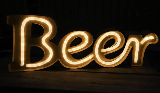 黄色霓虹啤酒标识与深色背景在一张木桌上图片下载