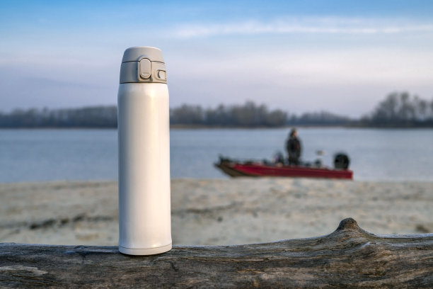 河边渔船模糊的背景上，倒在树上的白色热水瓶图片下载