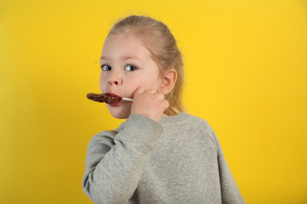 可爱的小女孩吃着黄色背景上甜甜的巧克力糖果。快乐的童年图片下载
