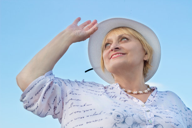 快乐微笑的退休女士拿着她的白帽子看天空图片下载