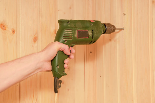 一个男人的手拿着一个旧的电钻，钻着一堵木板墙图片下载