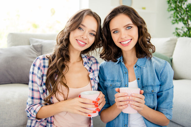 近距离的照片美丽的她，她的女士们的朋友们，伙伴们遇到热饮料，手，手臂，友好的心情，欣喜若狂，穿休闲牛仔裤，牛仔格子衬衫，公寓，坐地板沙发房间室内图片下载