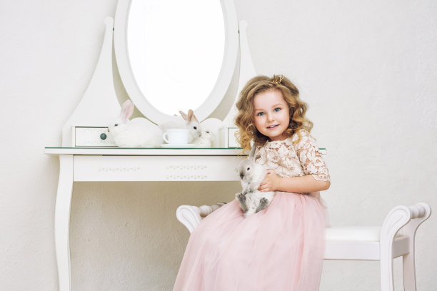 小女孩又漂亮又可爱，孩子穿着时尚的节日服装和带着动物的兔子在镜子里摆着白色的内饰图片下载