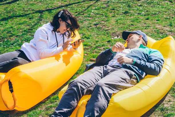 阳光明媚的日子，一对夫妇躺在城市公园的充气床垫上。说话和聊天图片下载