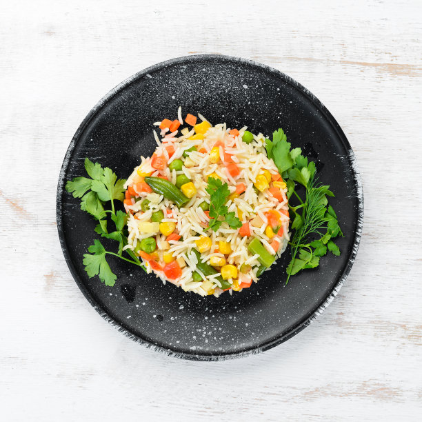 煮米饭和蔬菜。黑盘子里的意大利调味饭。前视图。免费空间。图片下载