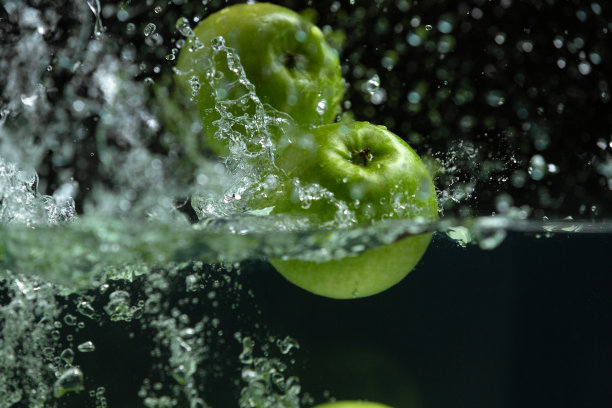 在黑色的背景下，新鲜的绿苹果飞溅到清澈的水中图片下载