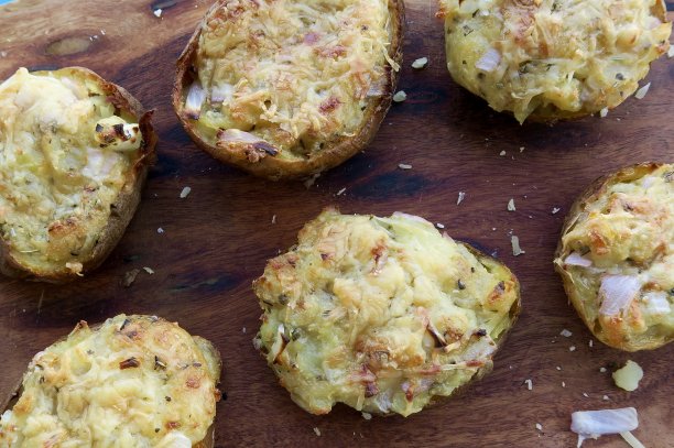 奶酪夹心土豆的图片，烤土豆塞满了奶酪和洋葱，放在厨房的木切菜板上烤图片下载