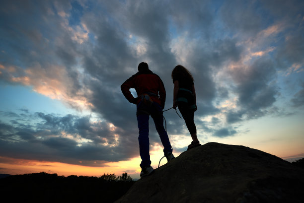 男男女女在岩石顶上看日落。以戏剧性的天空为背景的背面视图。图片下载