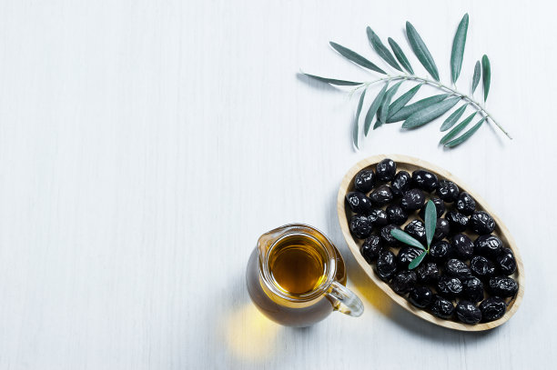 玻璃瓶自制橄榄油和橄榄枝，土耳其黑橄榄的种子和叶子放在白色的桌子上图片下载