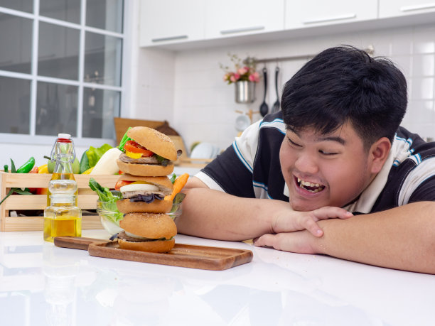 年轻的亚洲胖男人开心时，他吃不健康的食品或垃圾食品图片下载