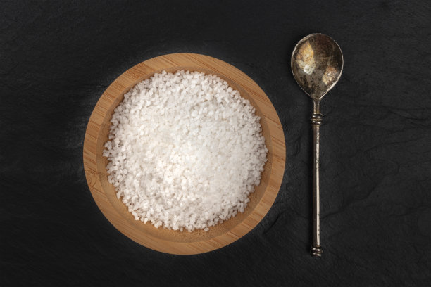 一碗海盐和一把勺子的照片，从顶部拍摄在一个黑色石板背景和文字的地方图片下载