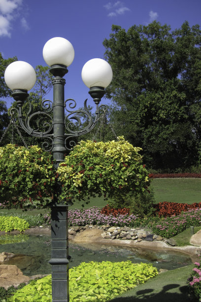 在阳光明媚的日子观赏正式花园，包括池塘、灯柱和花篮图片下载
