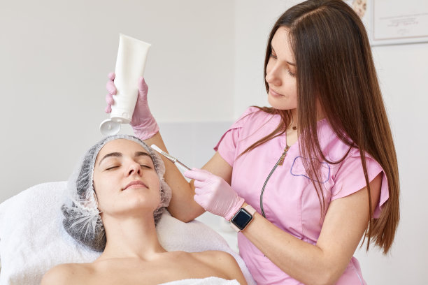 室内照片，美容师用刷子涂抹她的客户抗衰老面膜，手里拿着大瓶霜。女士闭上眼睛，在保湿和年轻化过程中放松。图片下载