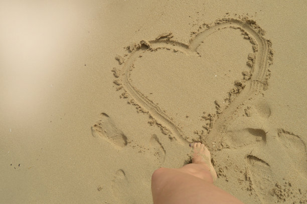 夏天你好，女人的脚站在沙滩上，在湿漉漉的沙滩上画了一个心形标志。休息、放松的概念，俯视图图片下载