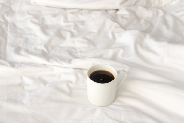 在舒适的早晨，黑咖啡杯放在未整理的床上，有复印空间。图片下载