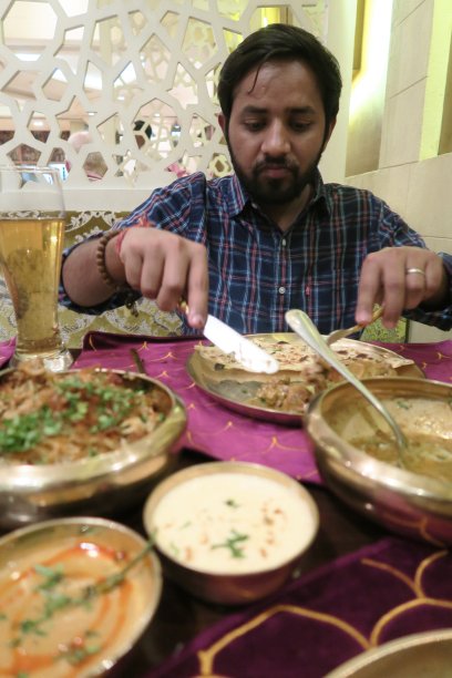印度男子在印度餐厅的餐桌上吃晚餐的照片，lucknowi鸡肉biryani，肉汁酱，raita，印度香菜米饭，香菜装饰，印度烤饼，mughlai reshmi鸡肉tikka烤肉串，品托照片，刀叉用餐照片图片下载